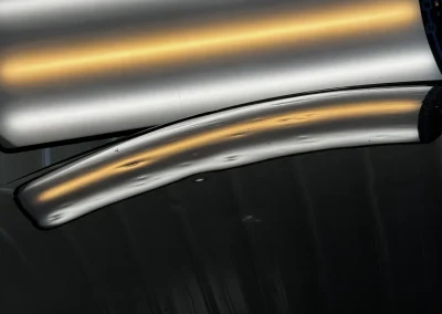 A close-up of a metallic surface with curved yellow reflections and small dents, set against a dark background.
