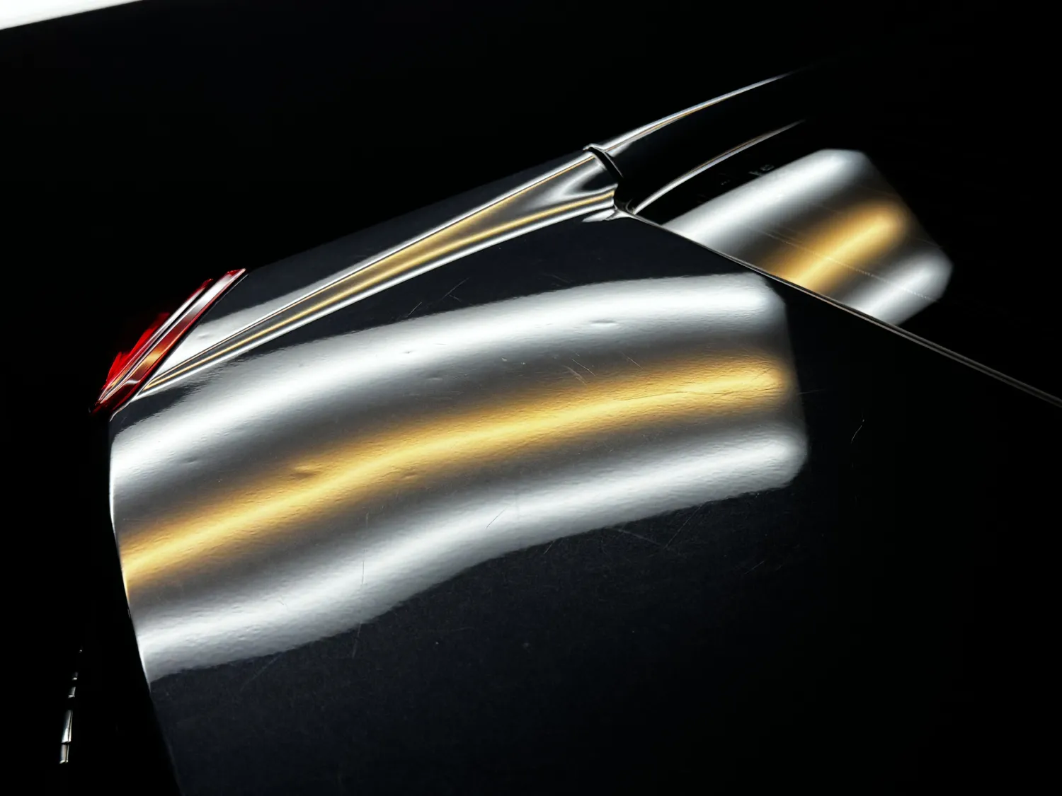 Close-up of a dark car hood with visible dents and reflections of overhead lights.
