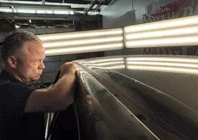 A man repairs a car roof under bright lights in a garage.