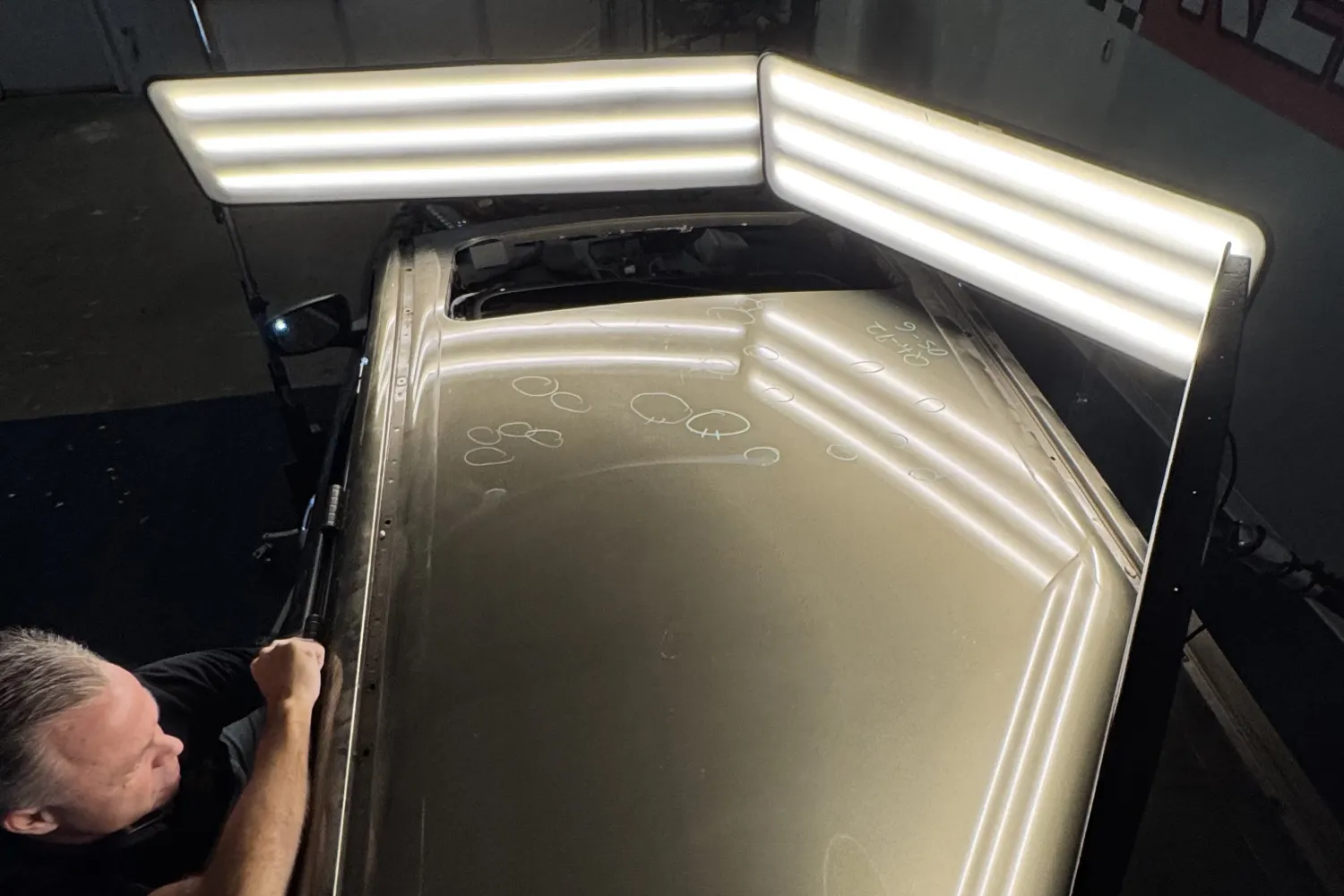 A man inspects a car roof with visible dents under bright inspection lights.