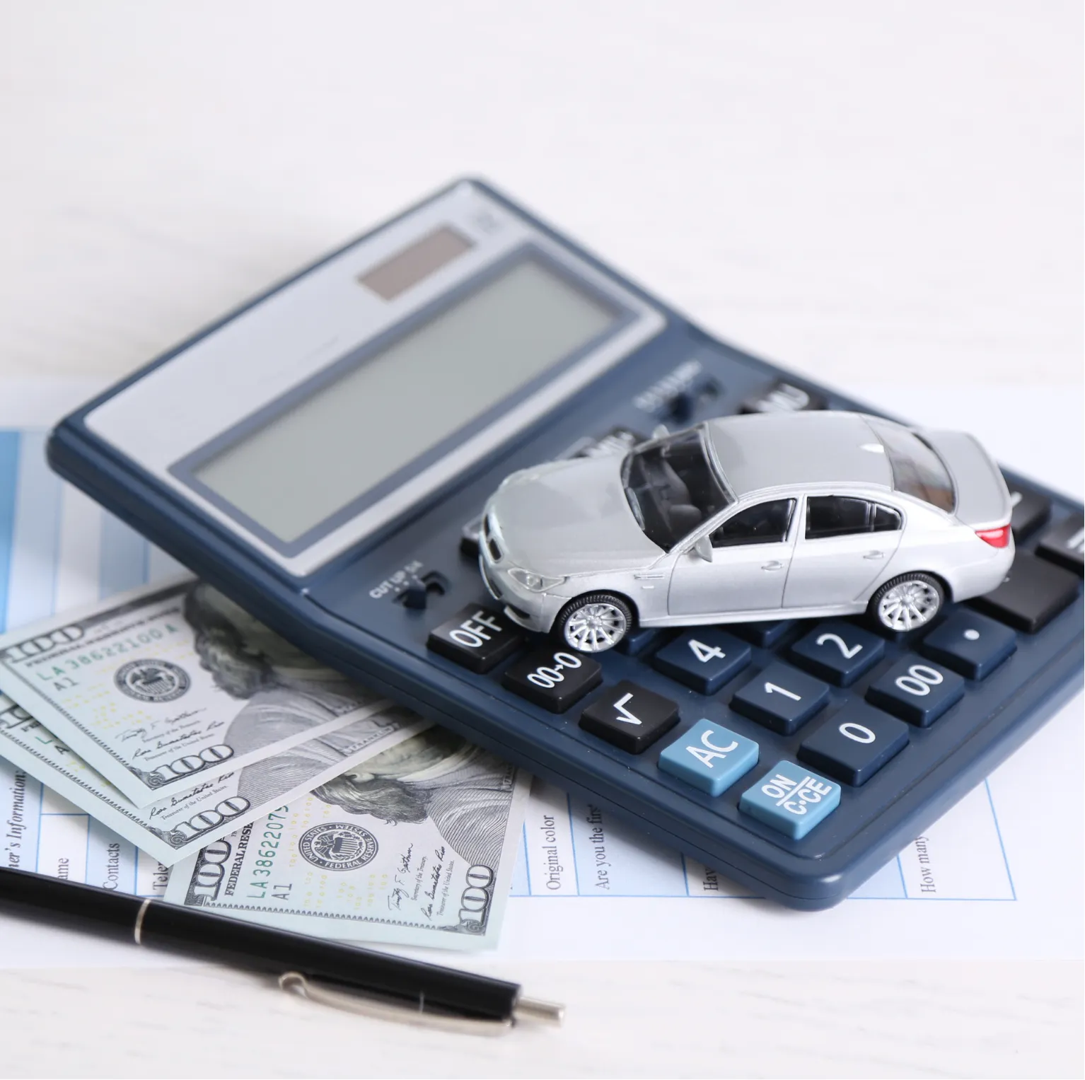 A toy car, cash, and documents on a calculator, symbolizing car finance or auto loan calculation.
