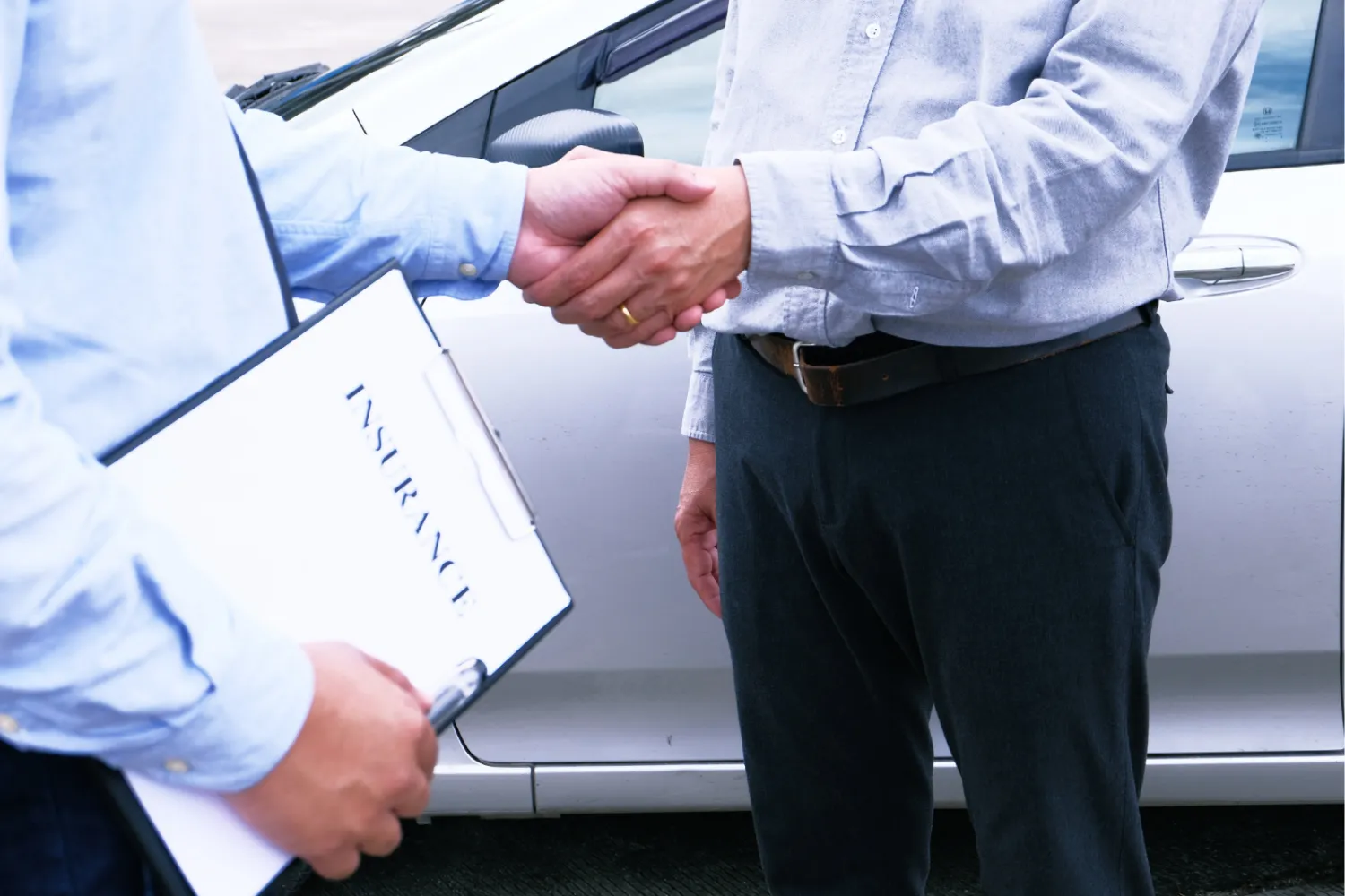 Two people shake hands near a car; one holds a clipboard labeled "insurance.