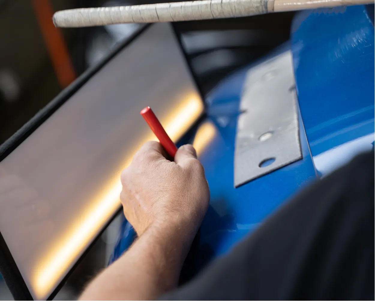 A person uses a red tool to repair a dent on a blue car with a reflective panel nearby.